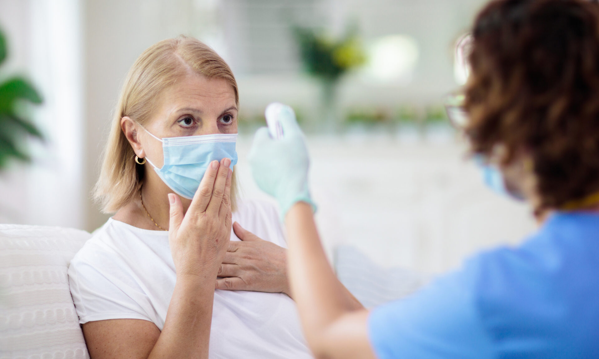 Nurse checking a masked COVID-19 patient's temperature